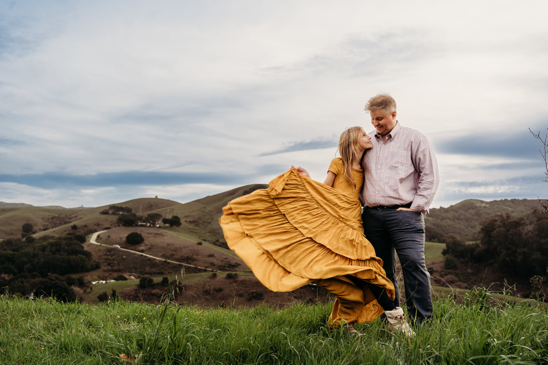 The father looks down as his daughter plays with her skirt during their family photos in the Pleasanton hills.