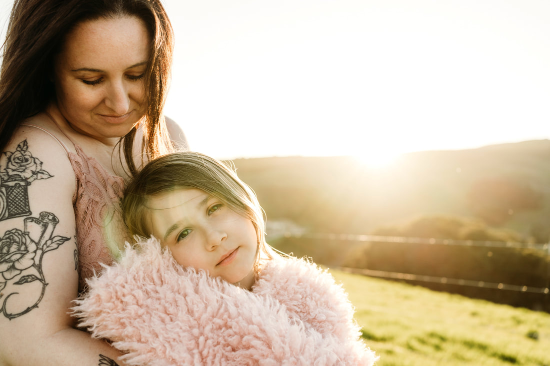 A girl gazes at the camera while her mother looks down at her during their golden hour family portrait session.