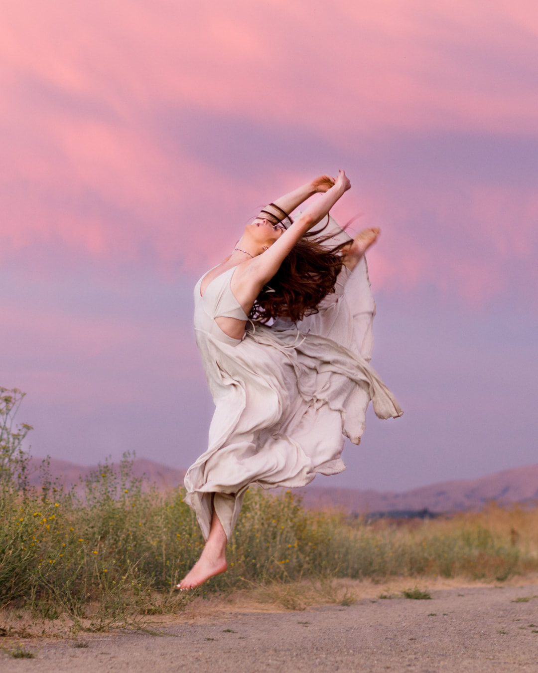 A ballet dancer, en pointe, with a magenta dress fluttering in the breeze on a sidewalk in San Ramon, CA