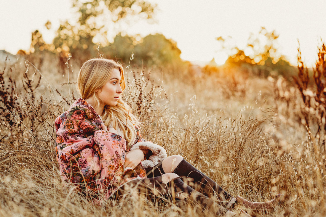 A high school senior girl gazing to the right while sitting in a field of golden grasses in Livermore.