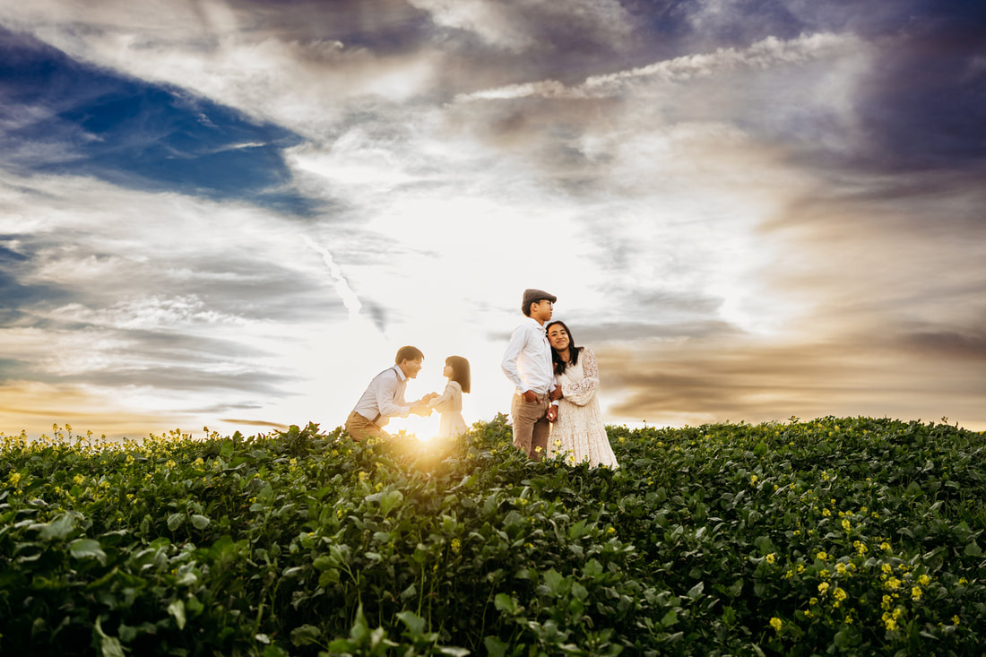A father and young daughter hold hands in a field of flowers in Pleasanton, CA while his wife and son look on.