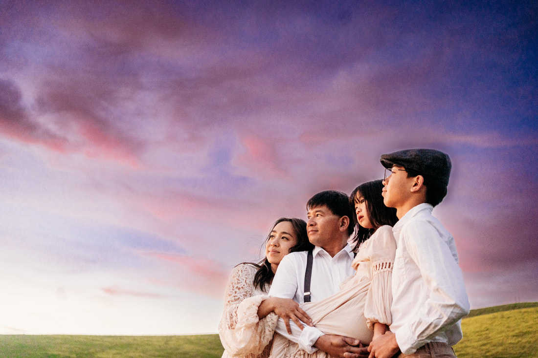 A family of four, standing together, gazing off towards the sunset with pink and purple clouds behind them.