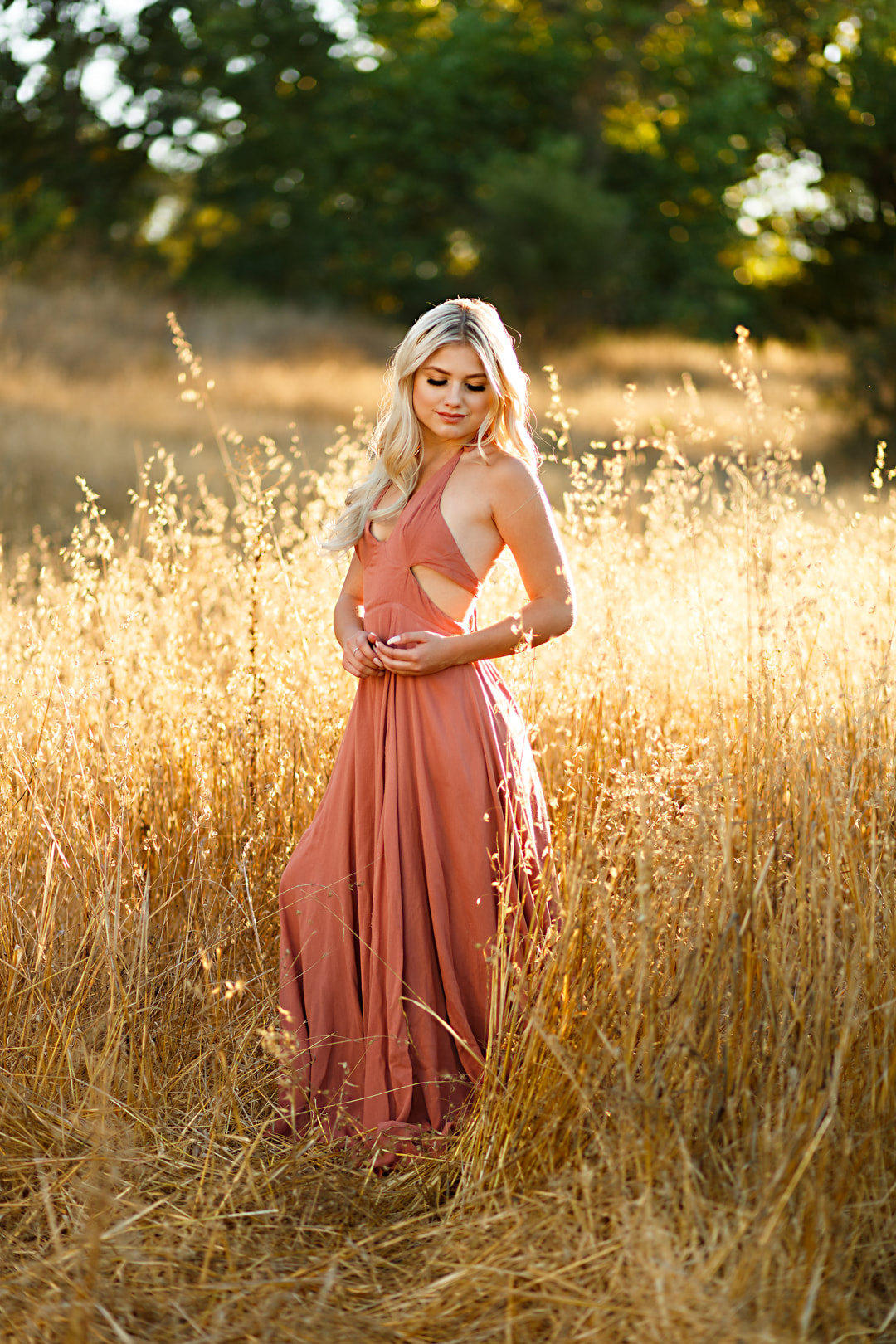 A high school senior girl looks down at the golden grasses surrounding her in this Livermore field