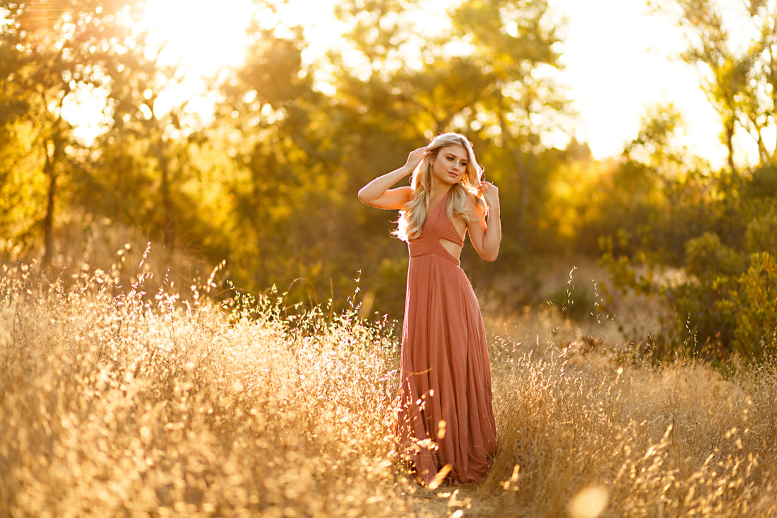 A girl in a pink dress stands in a field of golden backlit grasses in a field in Livermore