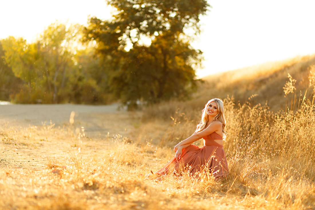 A girl in a pink dress sits on a log in a  field in Livermore