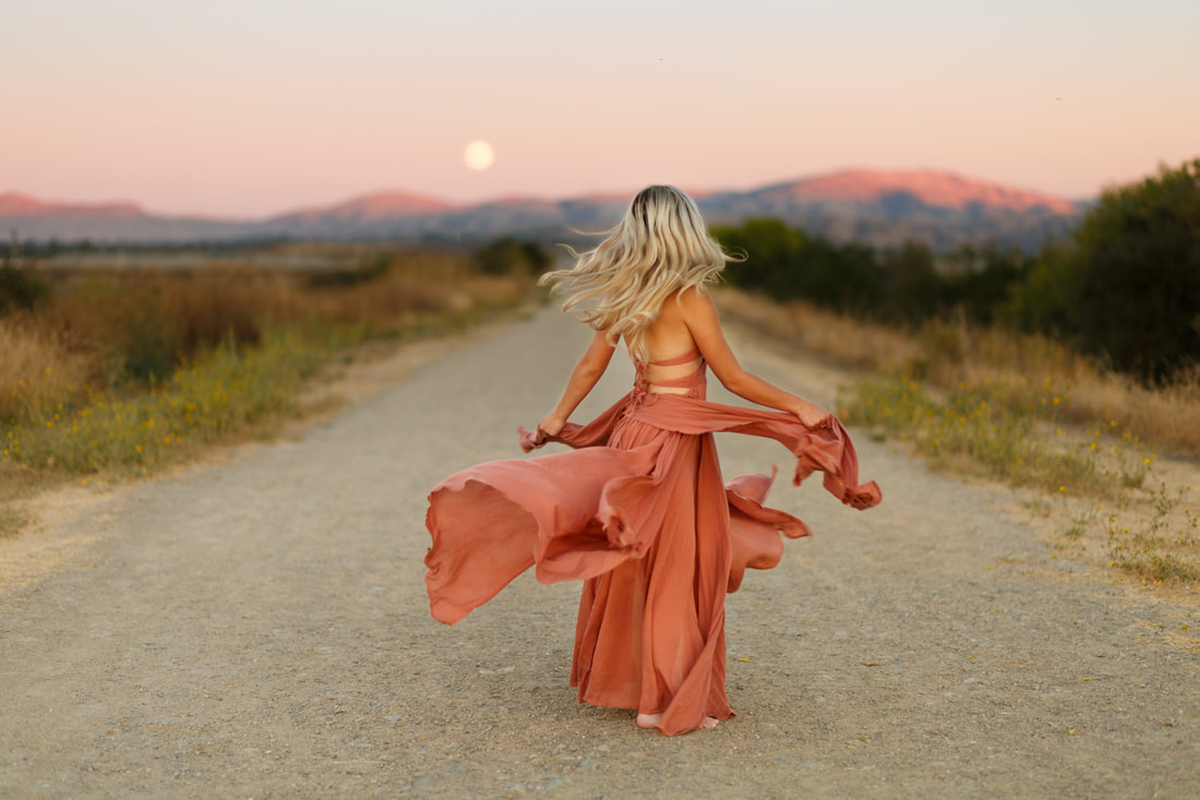 A high school senior girl faces away from the camera while her dress twirls in front of the Livermore hills
