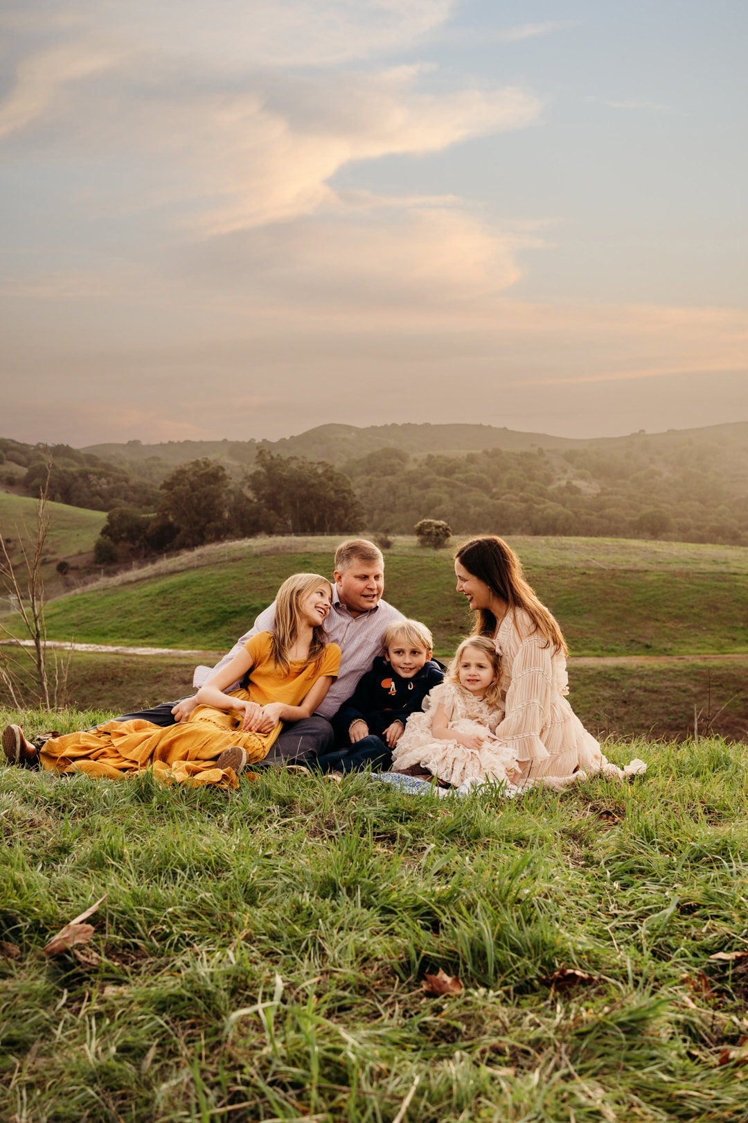 The sun sets behind the hills in Pleasanton as a family chats while sitting on a blanket.