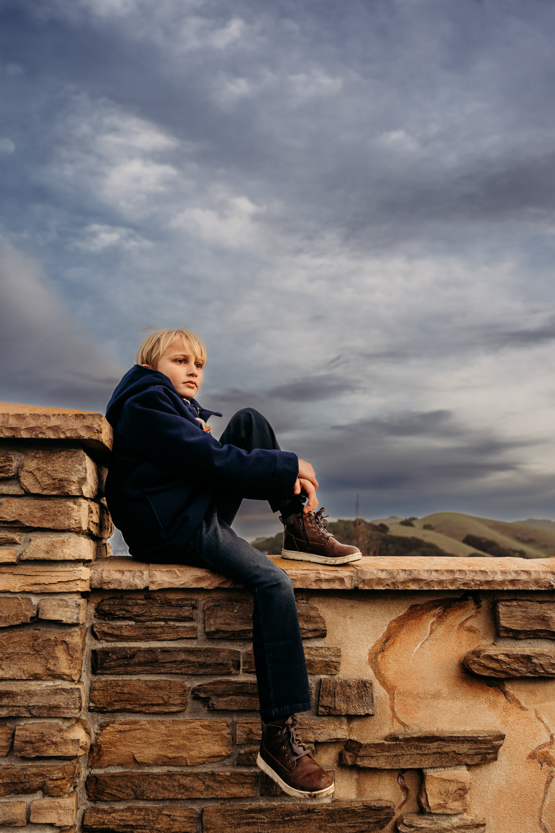 A quiet moment during family pictures when the son sits on a wall and gazes at the impending cloud line over the Pleasanton hills.